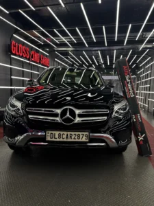 Black Mercedes-Benz SUV in a premium detailing studio with LED ceiling lights, showcasing AlfaShield Paint Protection Film box, highlighting high-gloss finish, car protection, and luxury detailing environment.