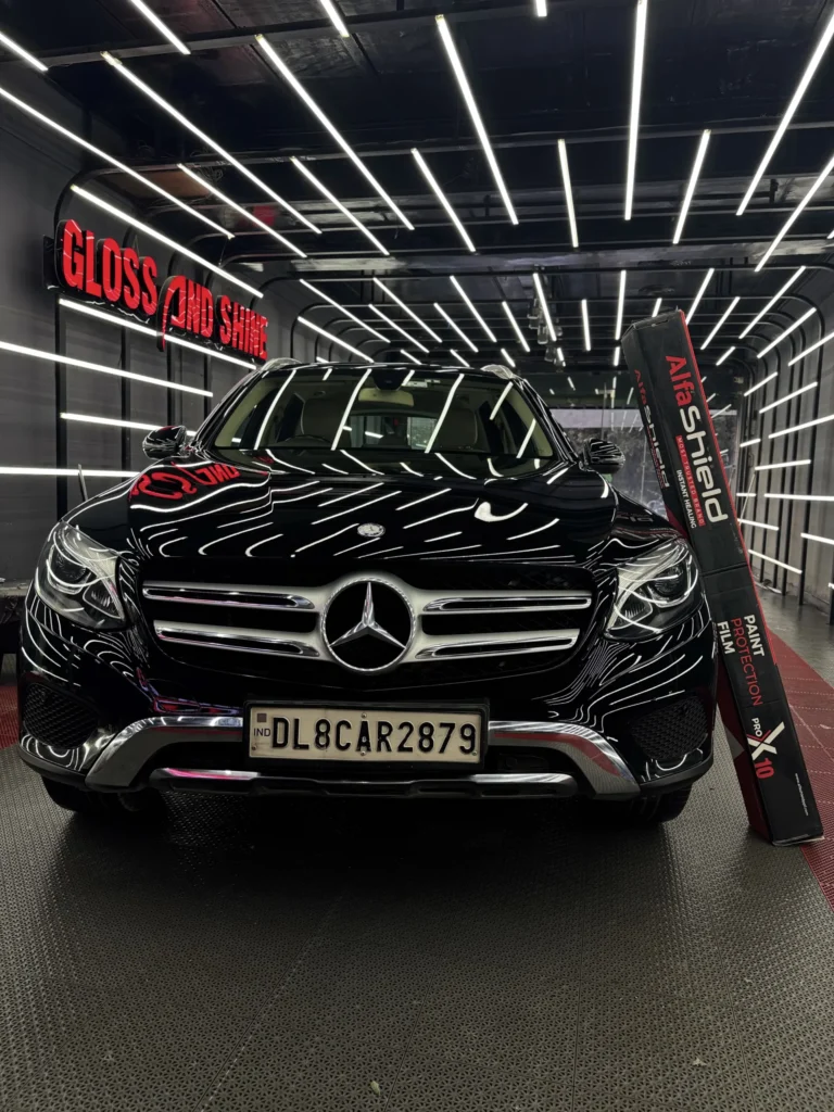 Black Mercedes-Benz SUV in a premium detailing studio with LED ceiling lights, showcasing AlfaShield Paint Protection Film box, highlighting high-gloss finish, car protection, and luxury detailing environment.